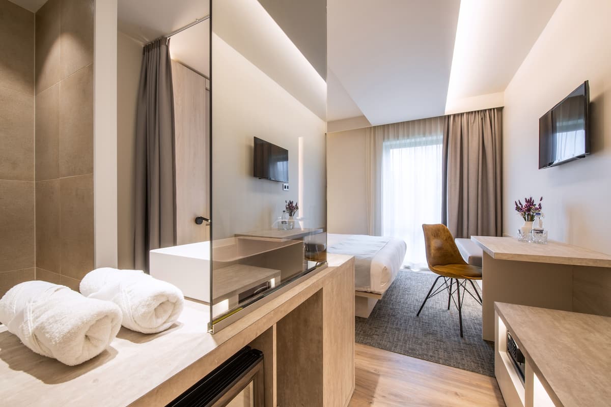 Quarto de hotel moderno com um espelho grande, uma cama, uma escrivaninha e uma cadeira.