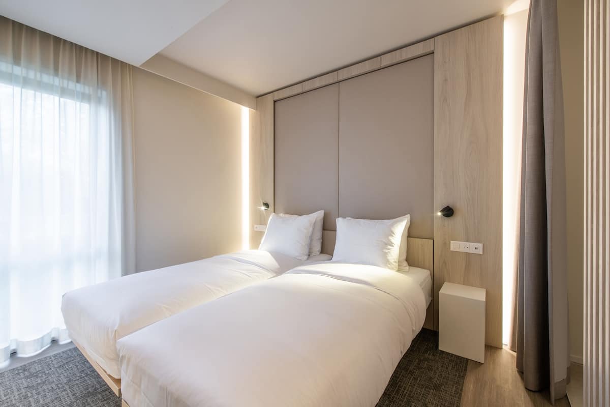 Quarto de hotel com uma cama grande, mesa de cabeceira e janela com cortinas.