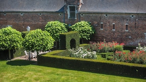 A brick building with a garden featuring hedges, a lawn, and red flowers. - Begijnhof Hotel (Leuven)