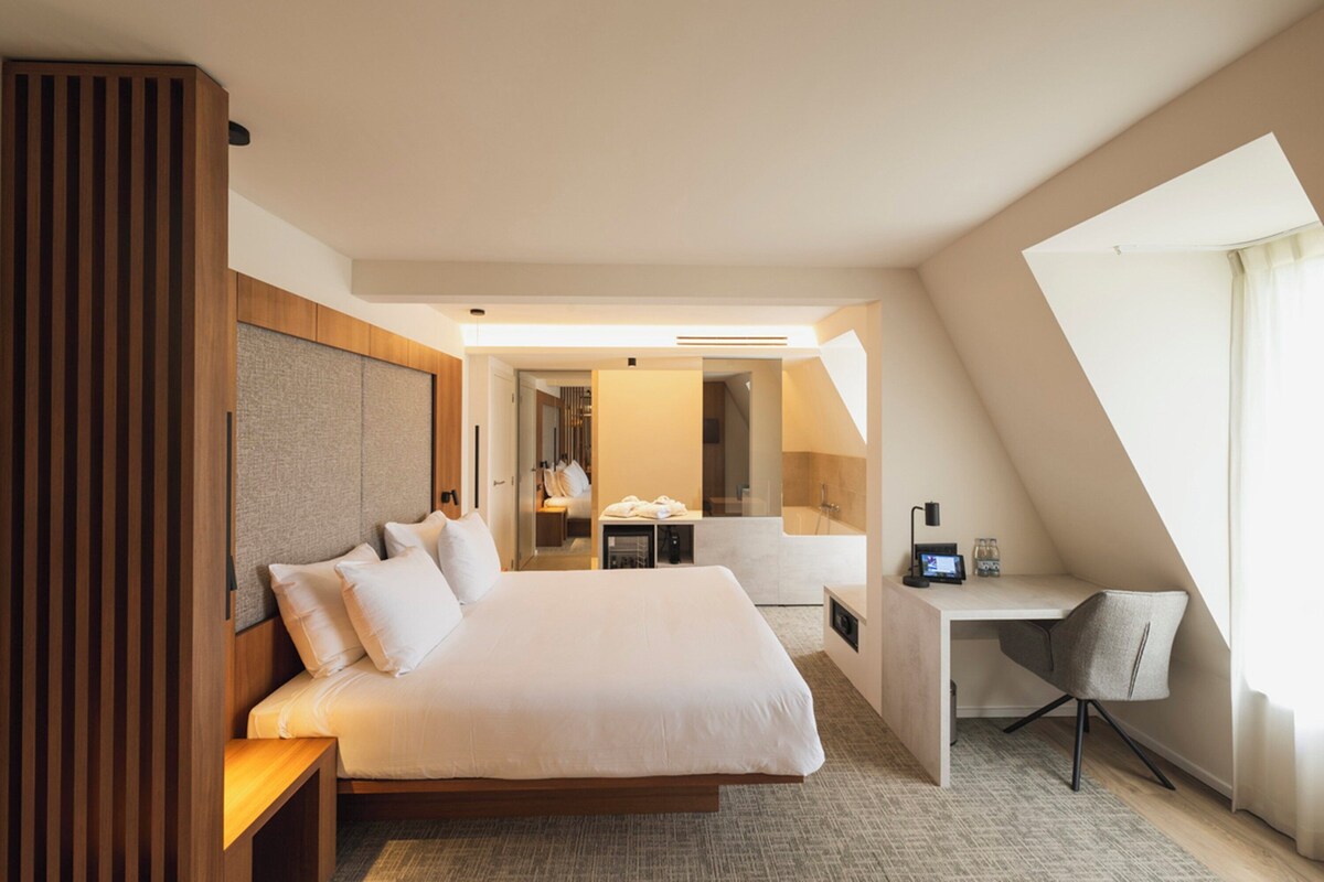 A modern hotel room with a large bed, a desk, and a shower area.