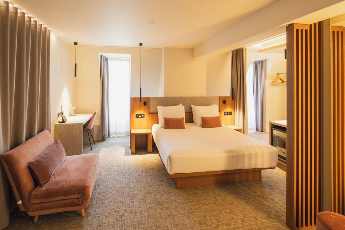 A hotel room with a large bed, a desk, a chair, and a sofa.