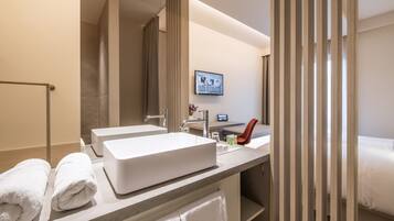 Een moderne hotelbadkamer met twee wastafels, een douche en een bed.