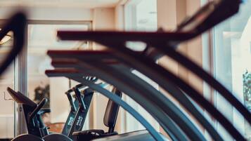 A row of stationary exercise bikes in a gym with large windows.