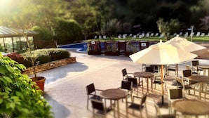 Un espace extérieur aménagé en terrasse, avec des tables et des chaises rondes, entouré de plantes en pot et d’une piscine.