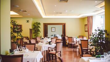 Un restaurante con varias mesas y sillas, suelo de madera y plantas en macetas.