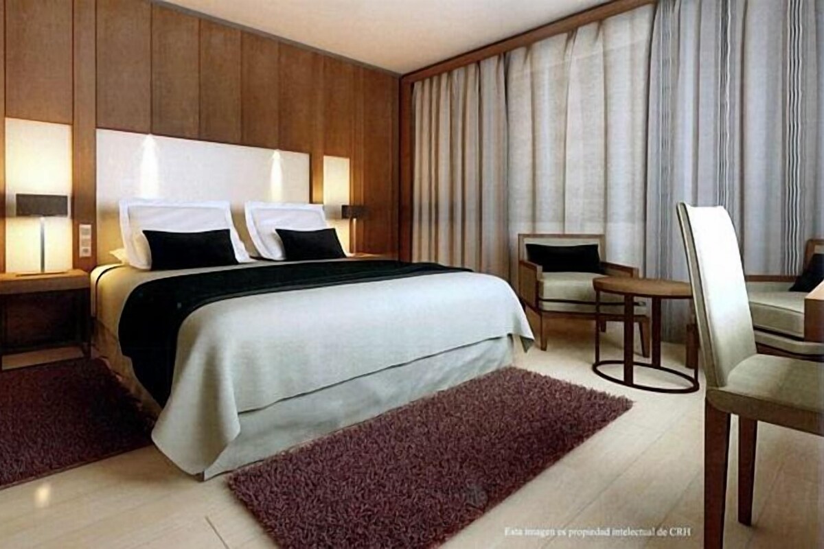 A modern hotel room with a large bed, two bedside tables, a desk, and a chair.