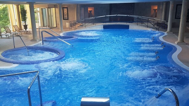 Une grande piscine intérieure dotée de plusieurs bains à remous et d’un élément décoratif central avec jeux d’eau.