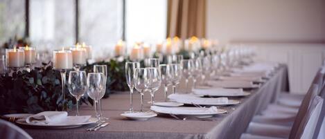 Una larga mesa de comedor con velas, copas de vino y platos listos para una comida.
