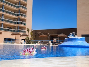 Una piscina de hotel con una fuente, sillas de descanso y sombrillas.