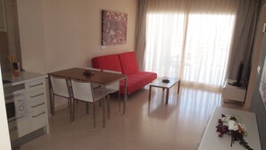 A modern living room with a dining area, a red sofa, a small table, and a painting on the wall. - Apartamentos Europa House Sun Beach (Guardamar del Segura)
