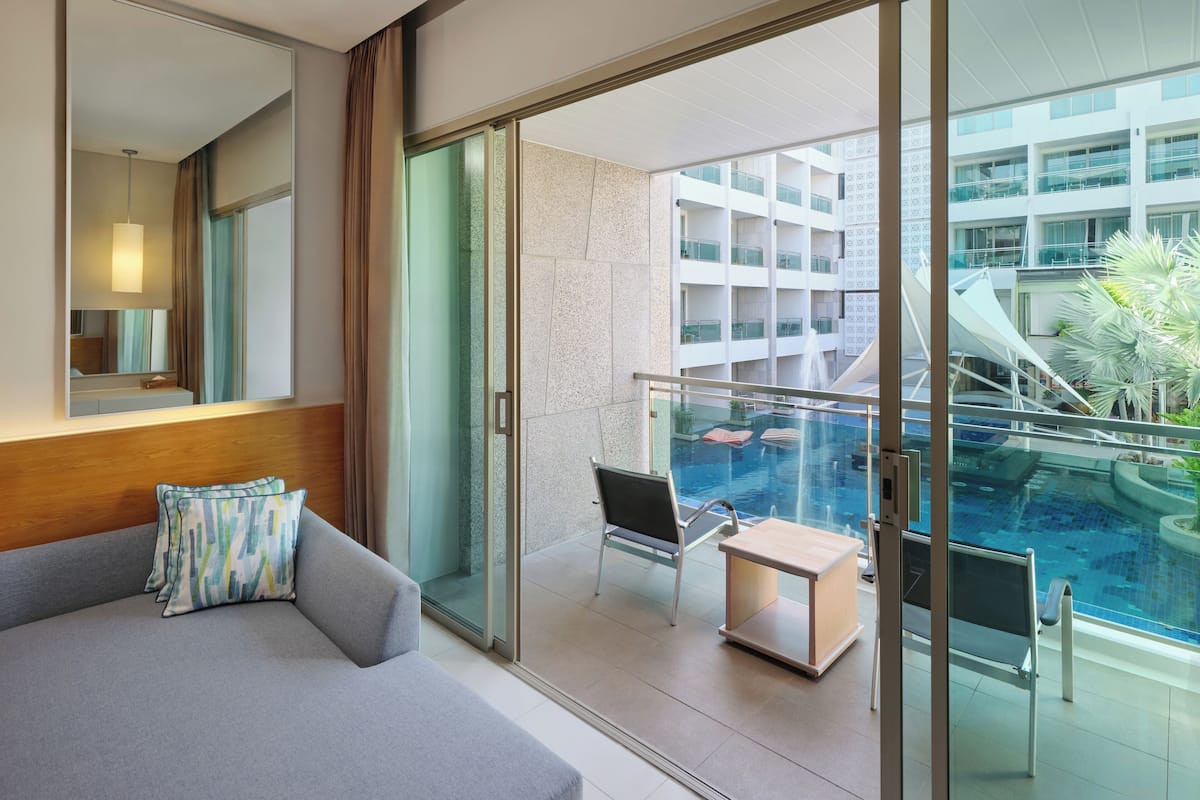 A modern hotel room with a balcony, a pool, and a view of the building's interior.