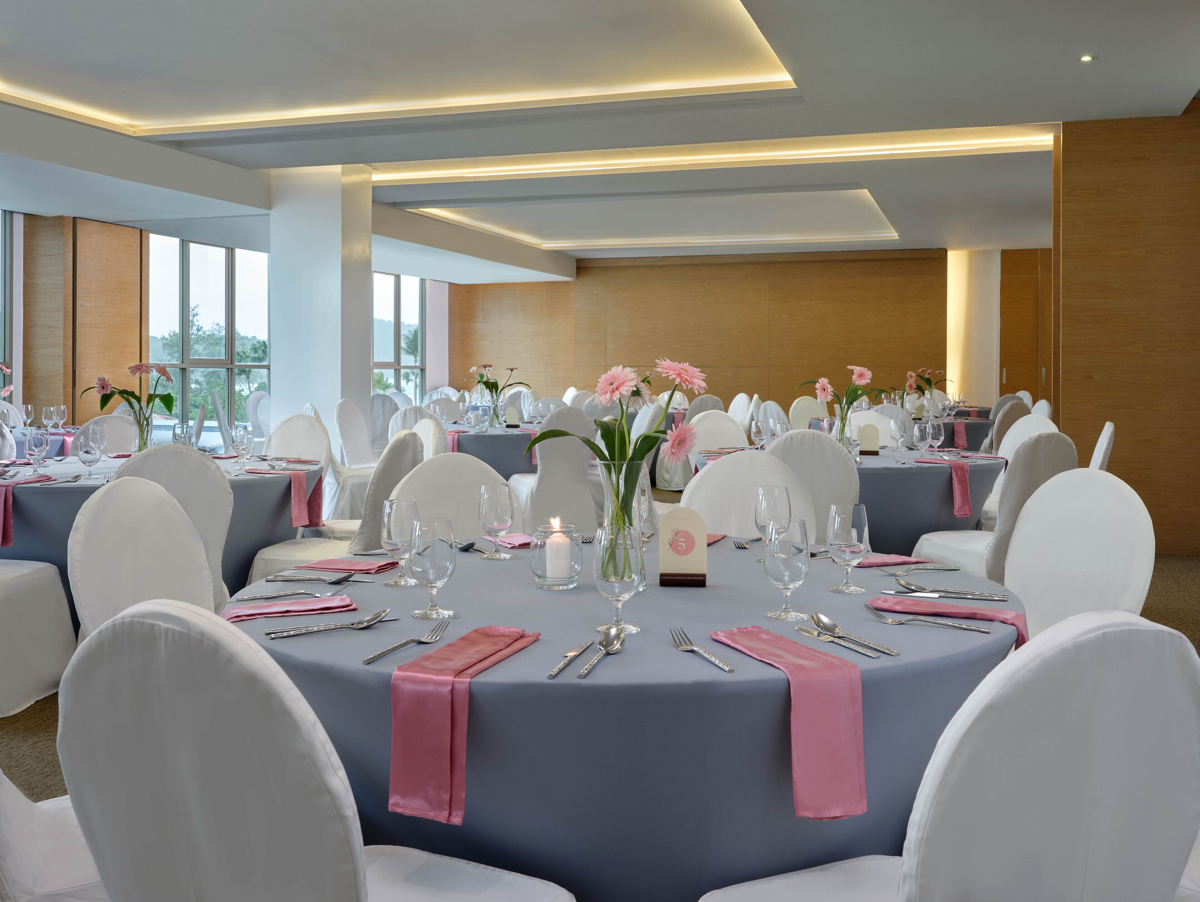 Une salle de banquet avec des tables rondes, des chaises blanches et des serviettes roses.