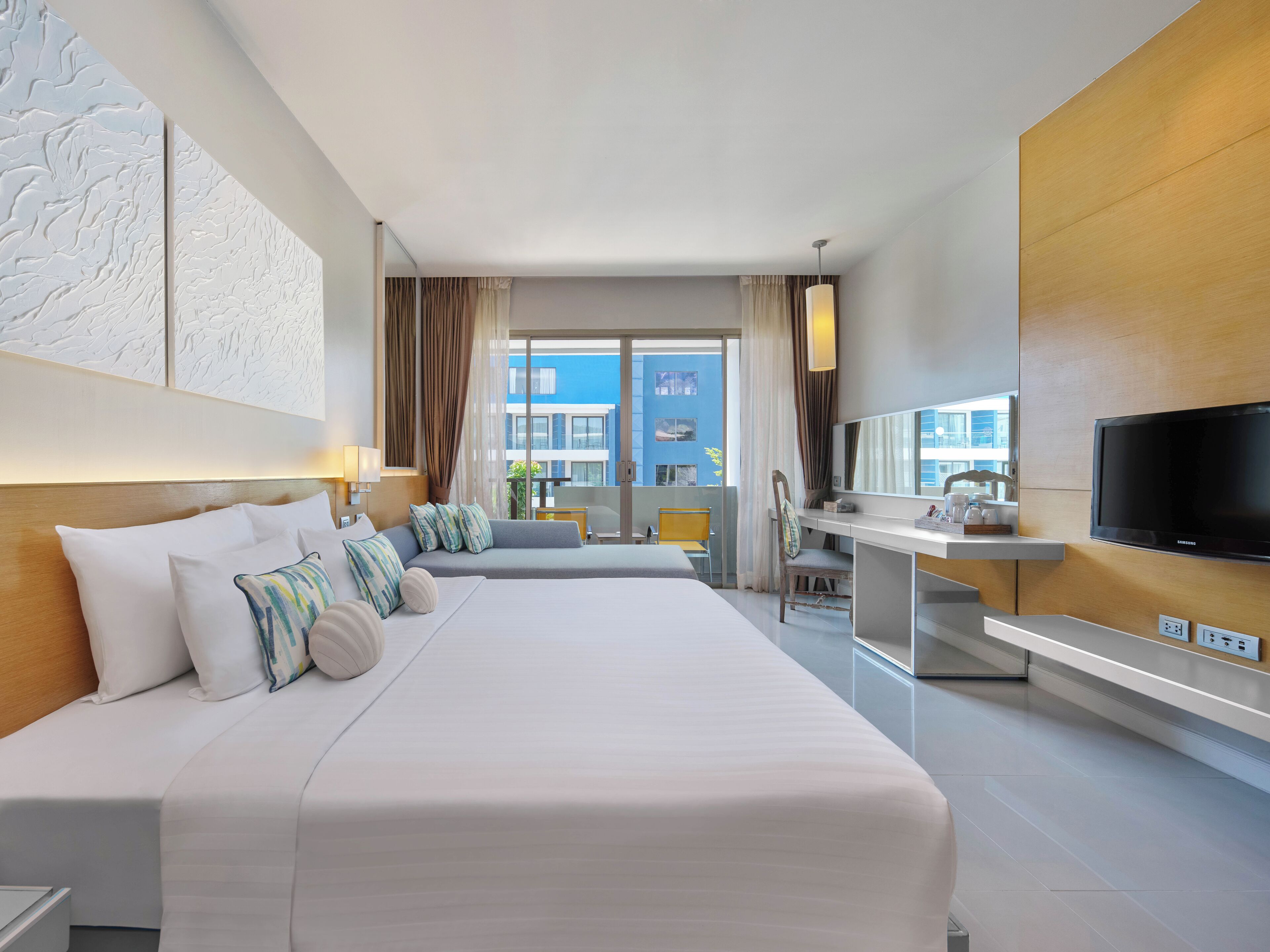 A modern hotel room with a large bed, a desk with a TV, and a view of the city.