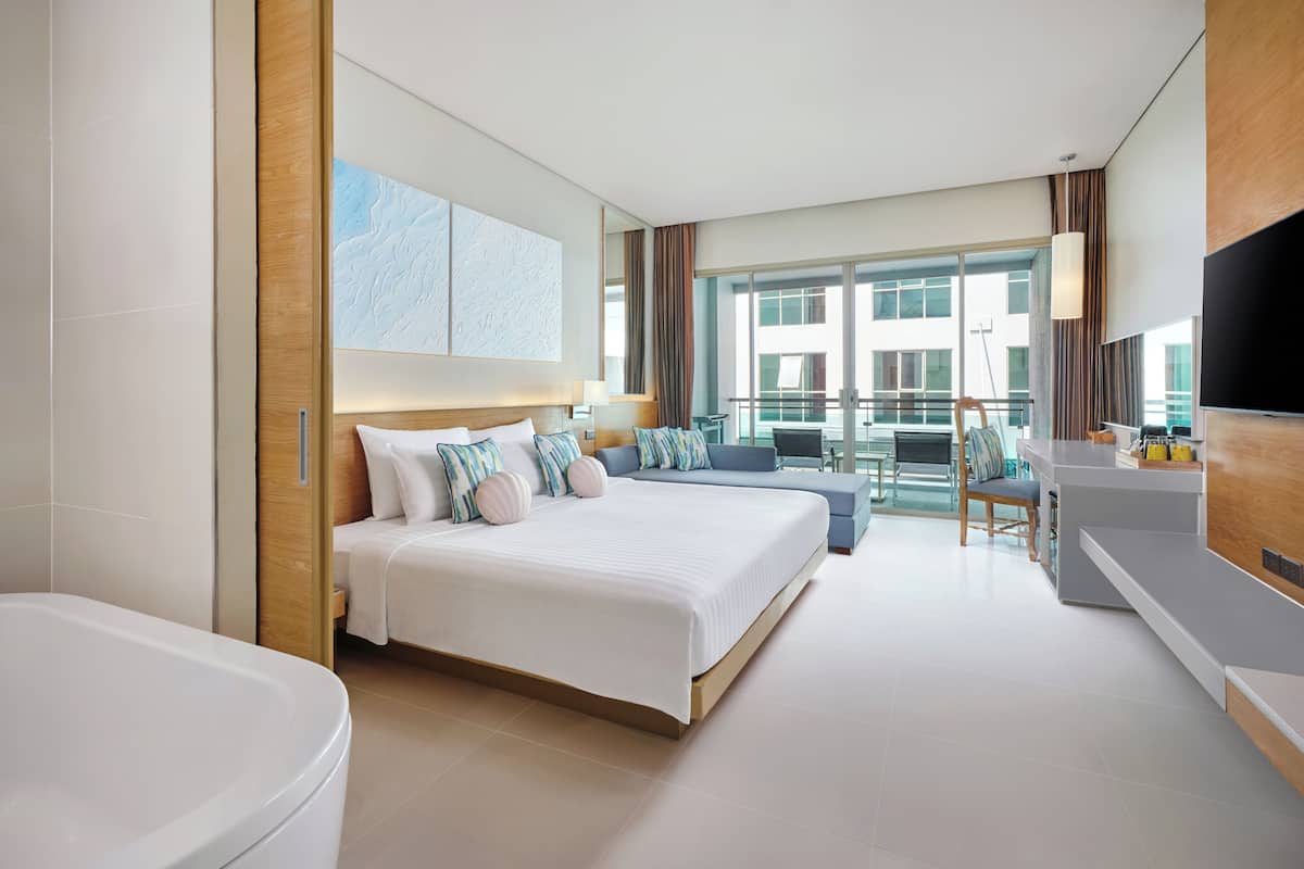 A modern hotel room with a large bed, a separate bathroom, a balcony with a view, and a flat-screen TV.