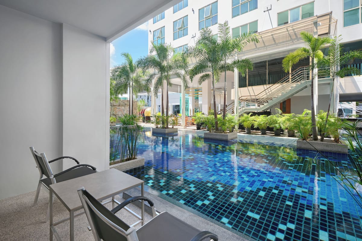 A modern hotel pool area with a tiled pool, outdoor seating, and palm trees.
