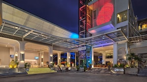 A modern hotel with a glass facade, outdoor seating, and a prominent digital display on the building. - The Kee Resort & Spa (Patong)