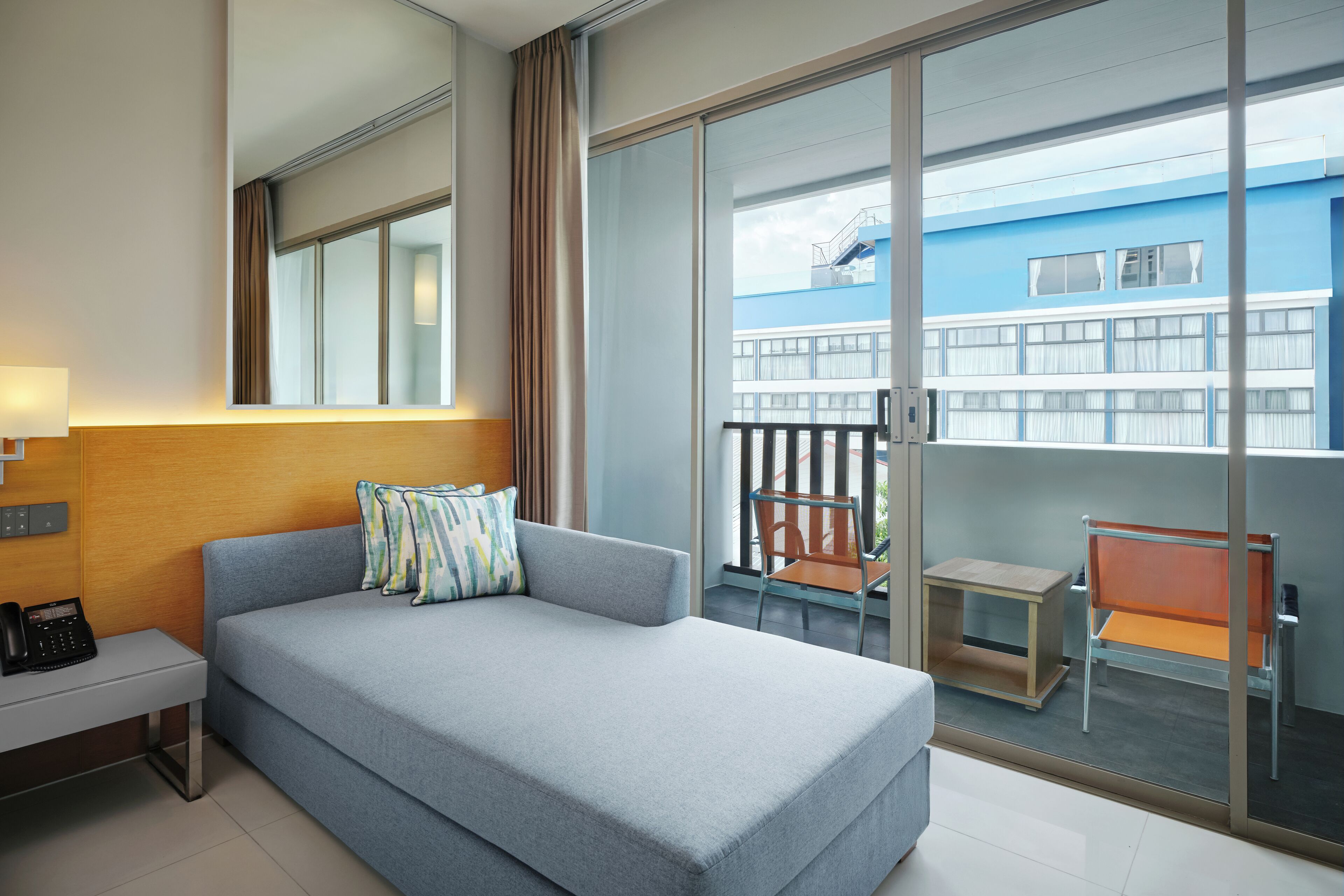 A hotel room with a bed, a desk, a chair, and a balcony with a view of a building.