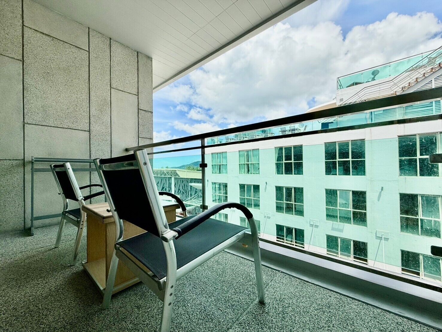 Un balcón con dos sillas y una pequeña mesa, con vista a un edificio con varias ventanas.