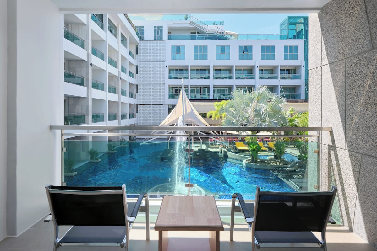 A balcony with a glass railing overlooking a swimming pool and a modern building complex.