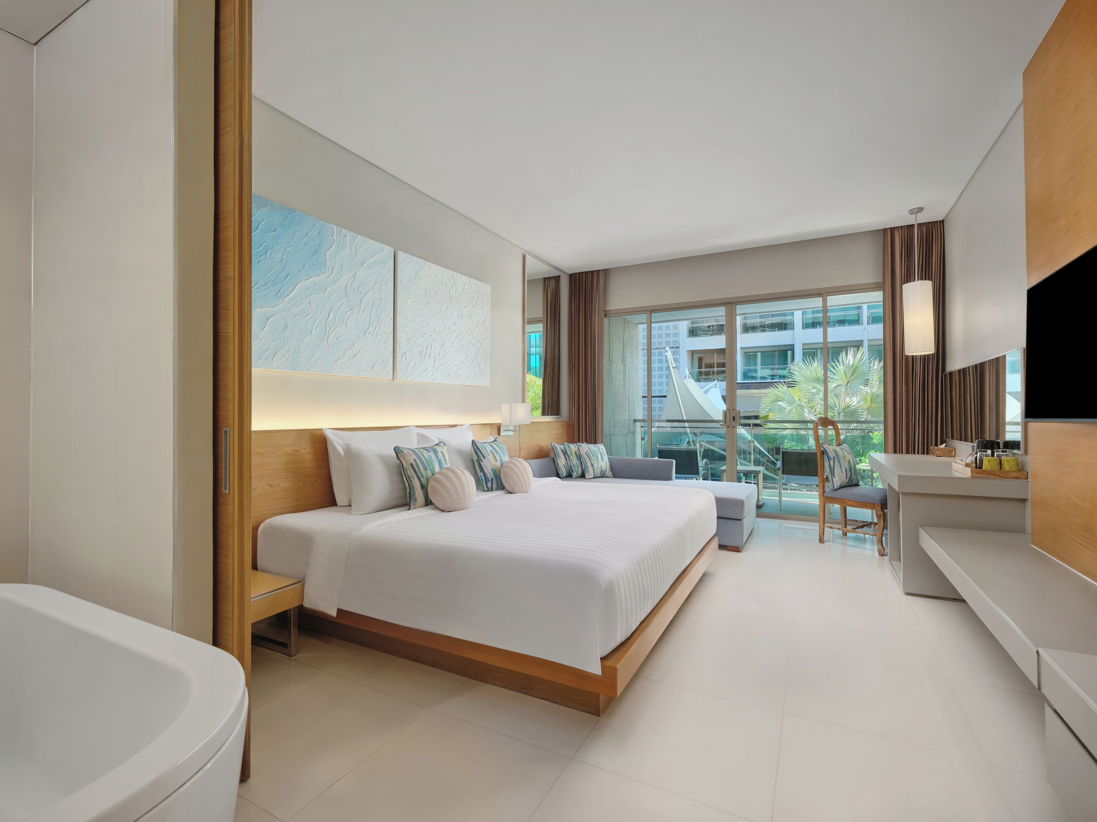 A modern hotel room with a large bed, a sitting area, a desk, and a view of the city.