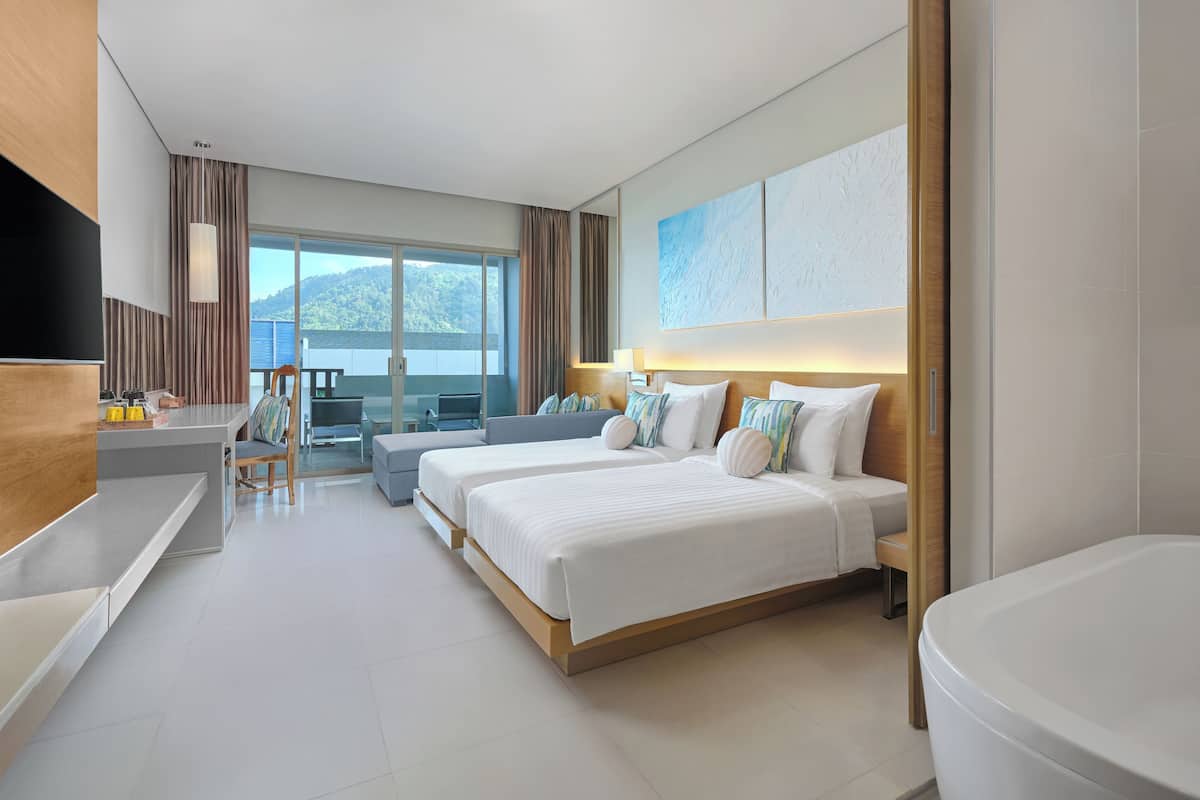 A modern hotel room with two beds, a desk, and a large window offering a view of the outdoors.