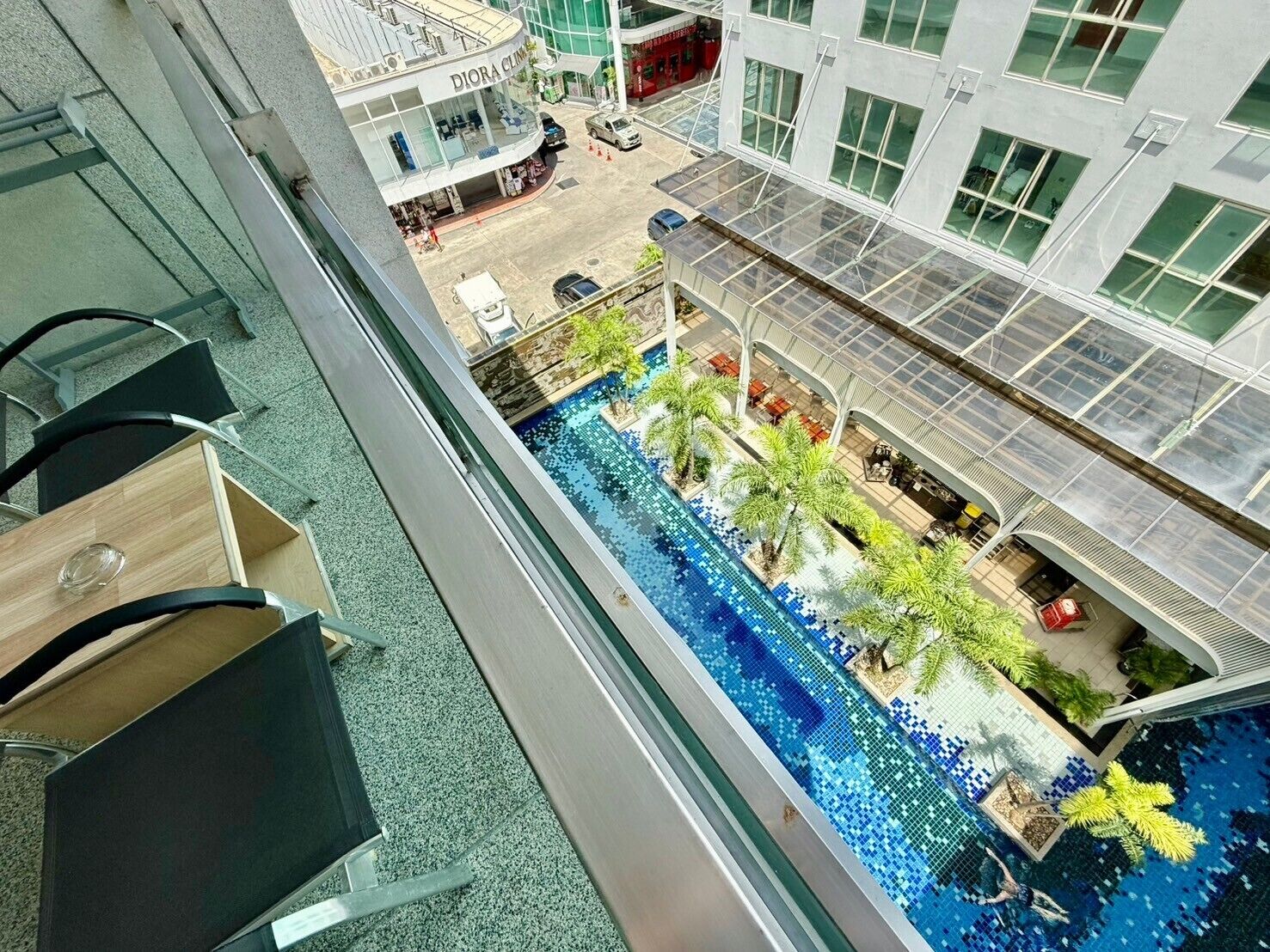 Uitzicht op een zwembad met palmbomen, een glazen balustrade en een gebouw op de achtergrond.
