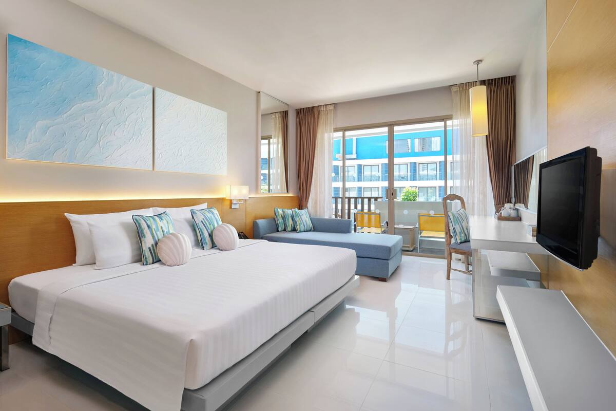 A hotel room with a large bed, a sofa, a desk, and a TV.