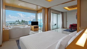 A modern hotel room with a large bed, a TV, a bathtub, and a balcony with a view of the ocean. - The Kee Resort & Spa (Patong)