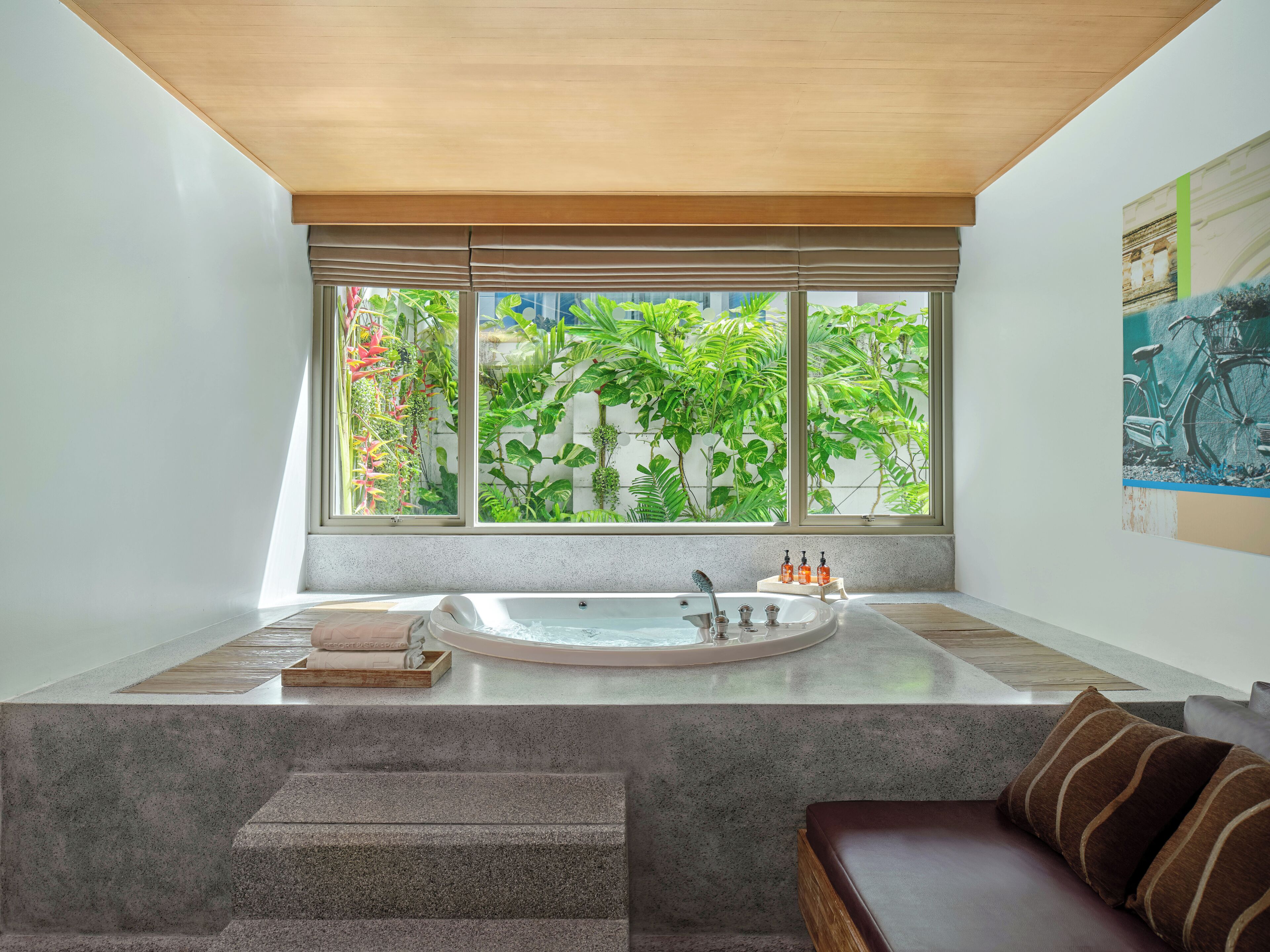 A modern bathroom with a freestanding bathtub, a sink, and a window with a view of lush greenery.