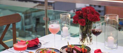 A table set for a meal with dishes, drinks, and flowers, overlooking a scenic view.