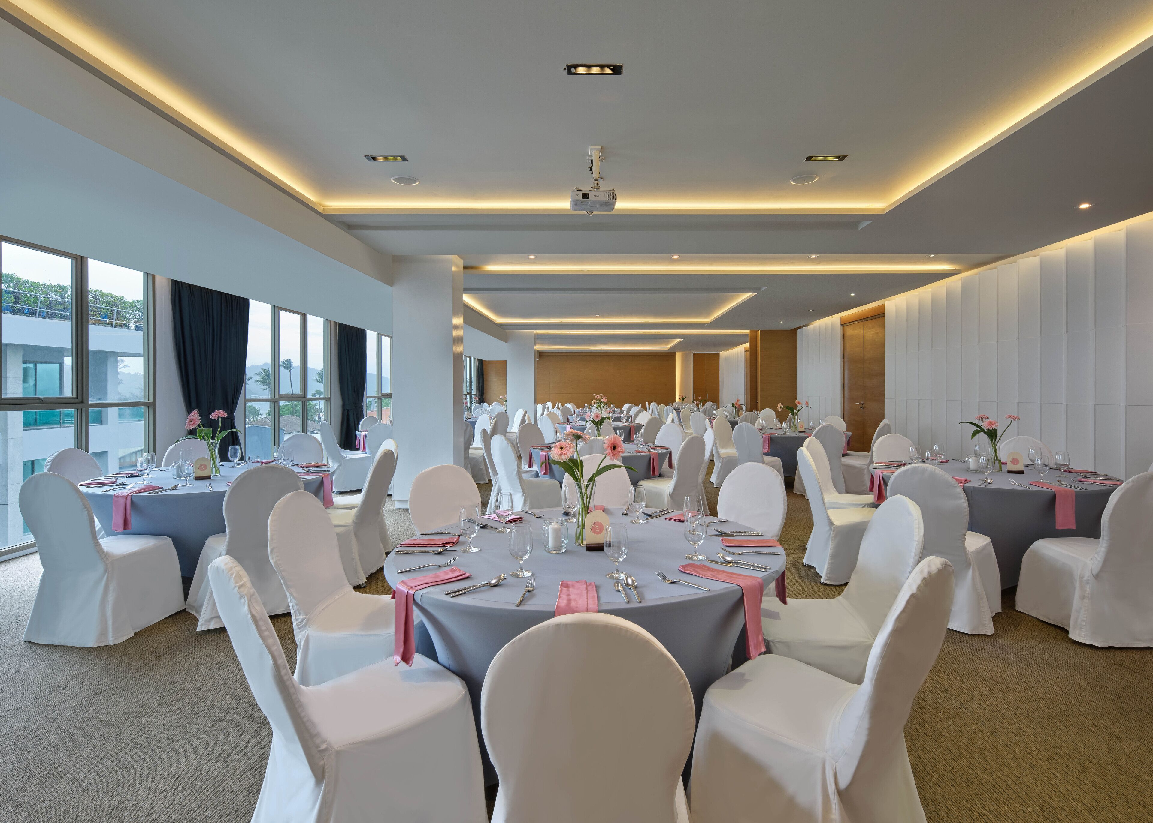 A banquet hall with round tables, white chairs, and floral centerpieces.