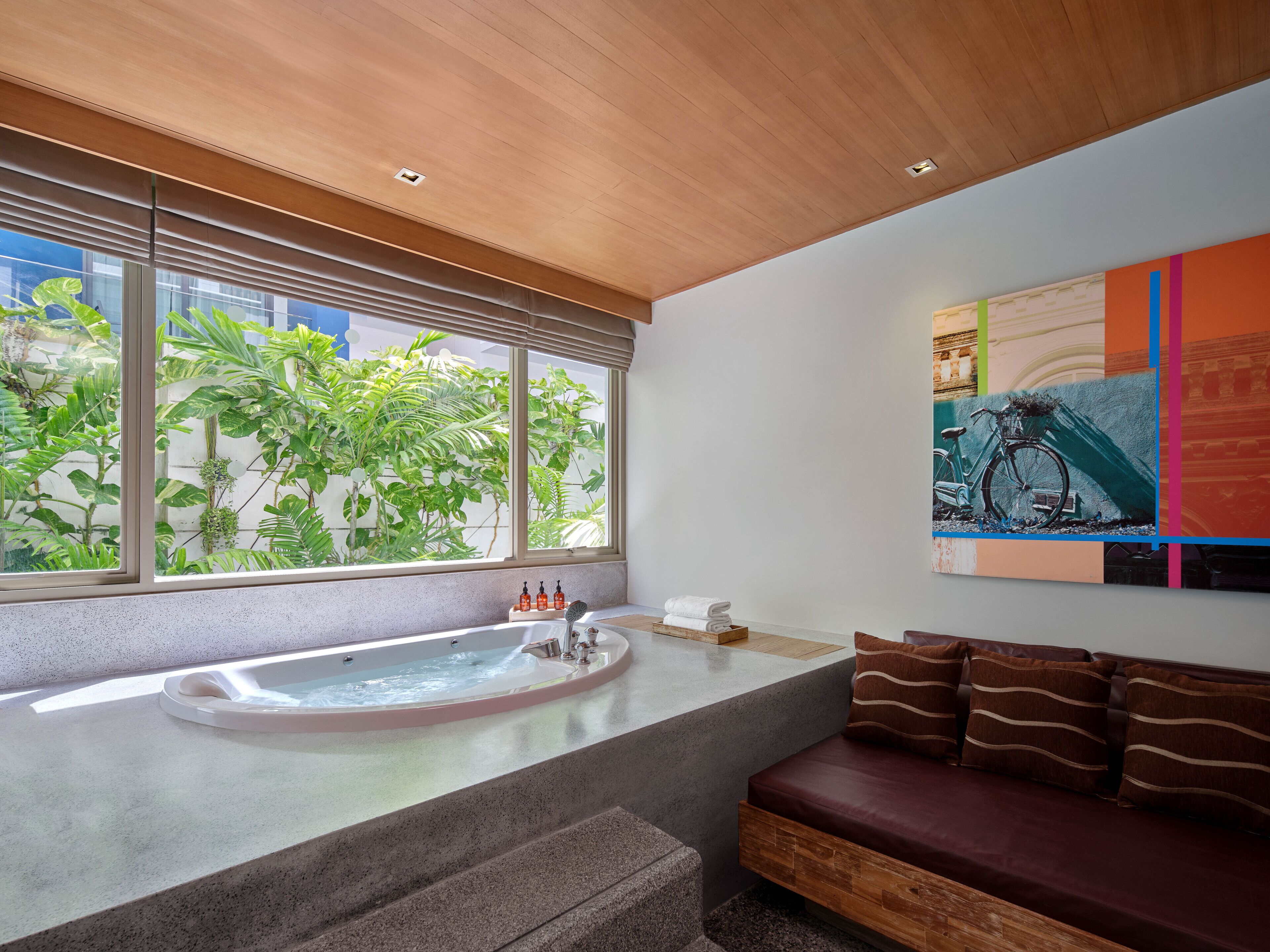 A modern bathroom with a bathtub, a wooden ceiling, and a large window with plants.