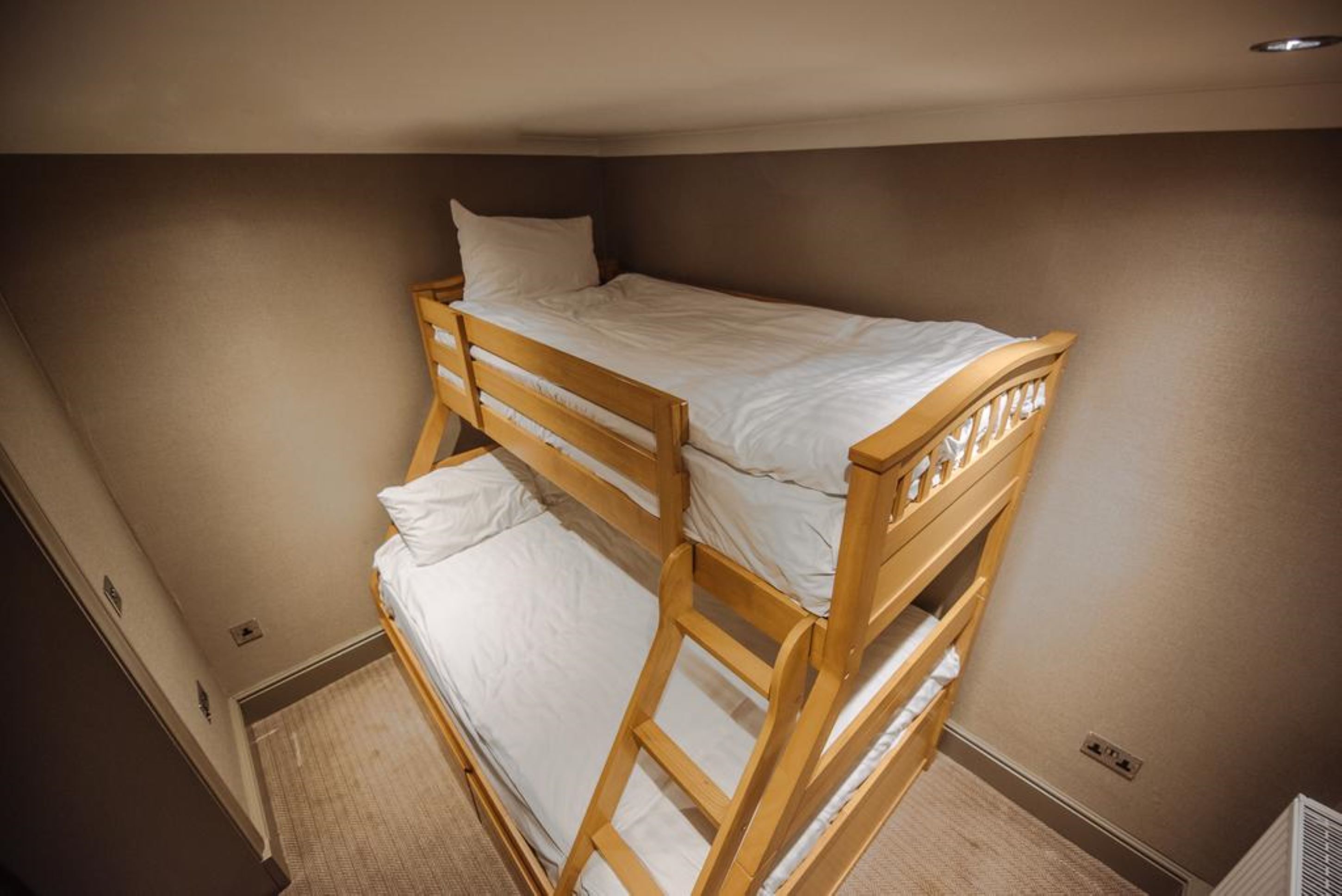 Una cama litera con ropa de cama blanca en una habitación con paredes color beige y piso alfombrado.