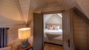 A bedroom with a sloped ceiling, a bed with white bedding and orange pillows, a lamp on a bedside table, and wooden paneling. - Bowfield Hotel and Spa (Johnstone)