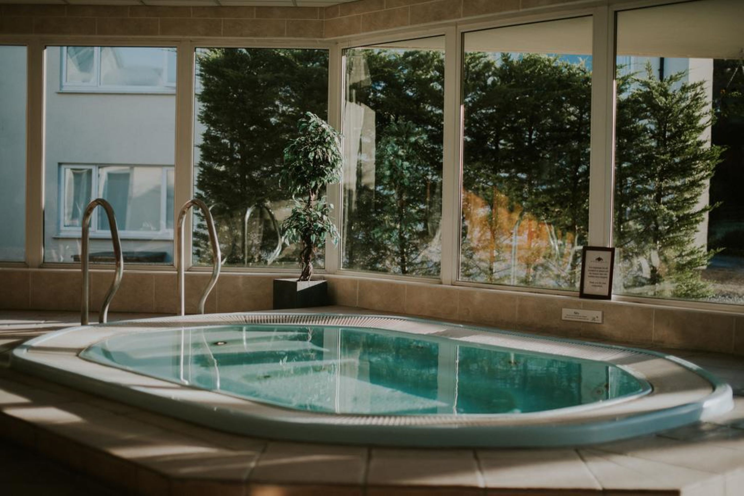 Piscina com água cristalina, rodeada por janelas amplas que oferecem vista para árvores e um edifício.
