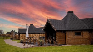 A row of wooden cabins with pitched roofs, a paved walkway, and a grassy area. - Bowfield Hotel and Spa (Johnstone)