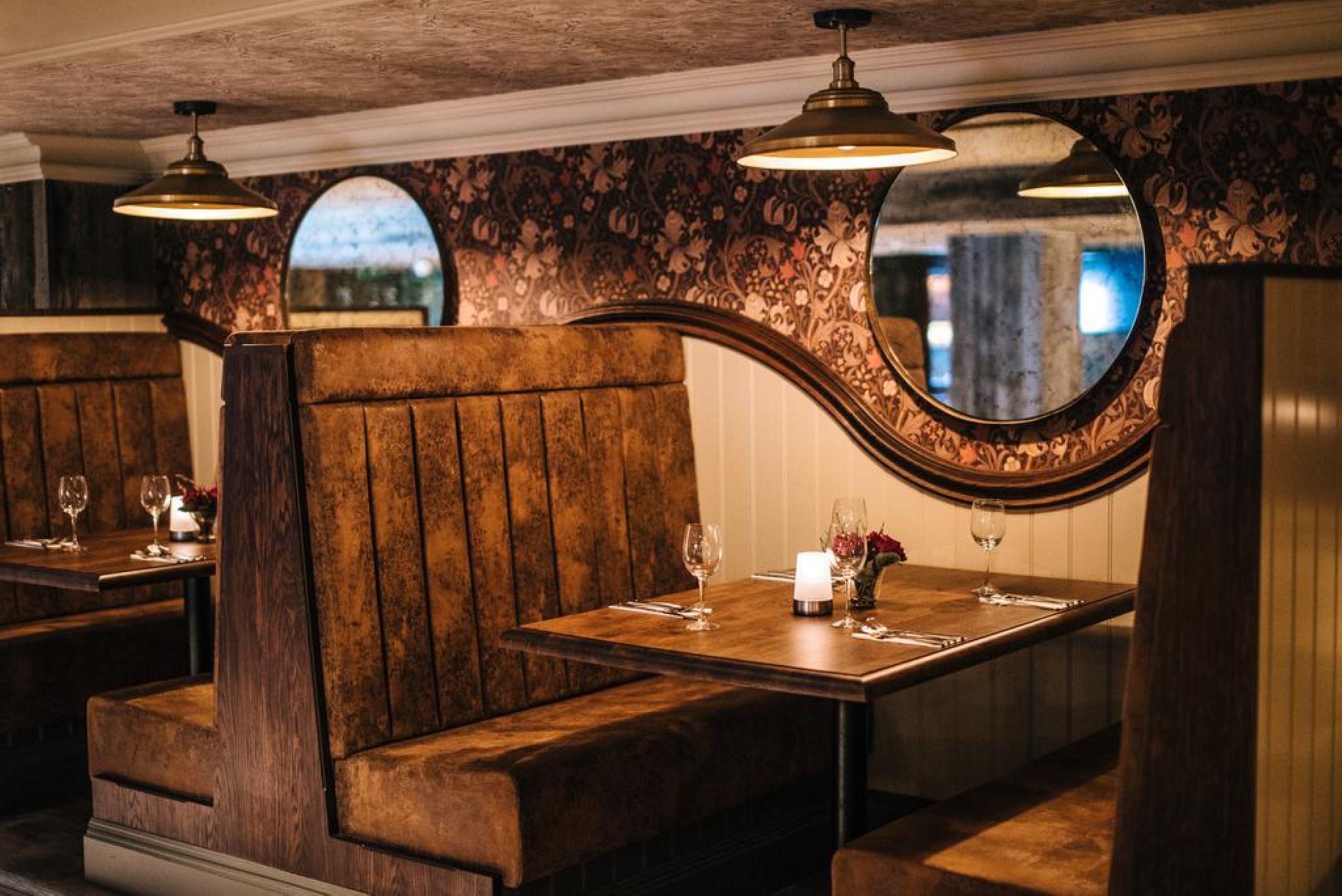 Un restaurante con cabinas de madera, un espejo y una mesa dispuesta con copas de vino y una vela.