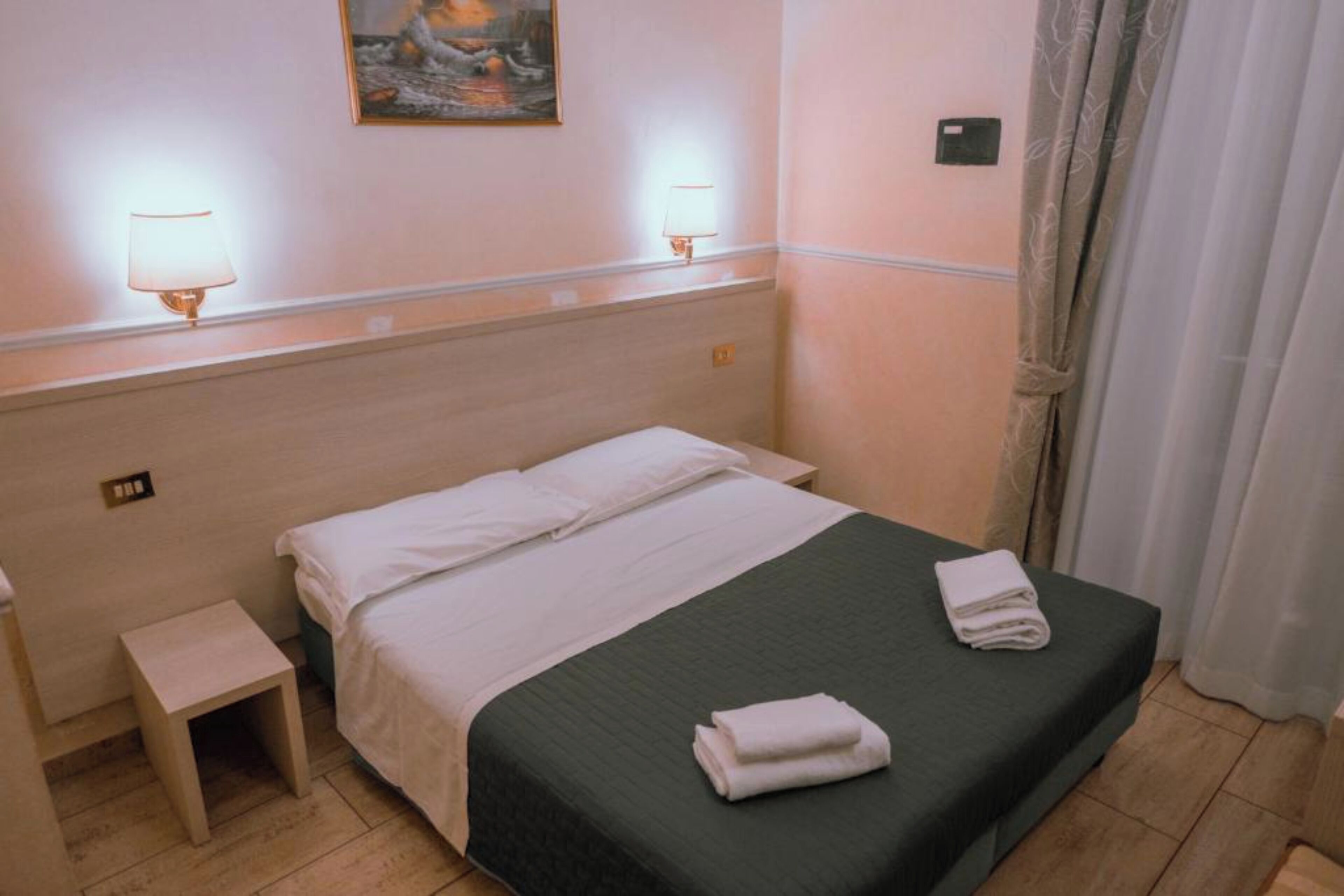 Ein Hotelzimmer mit Bett, Nachttischlampen, einem kleinen Beistelltisch und einem Bild an der Wand.