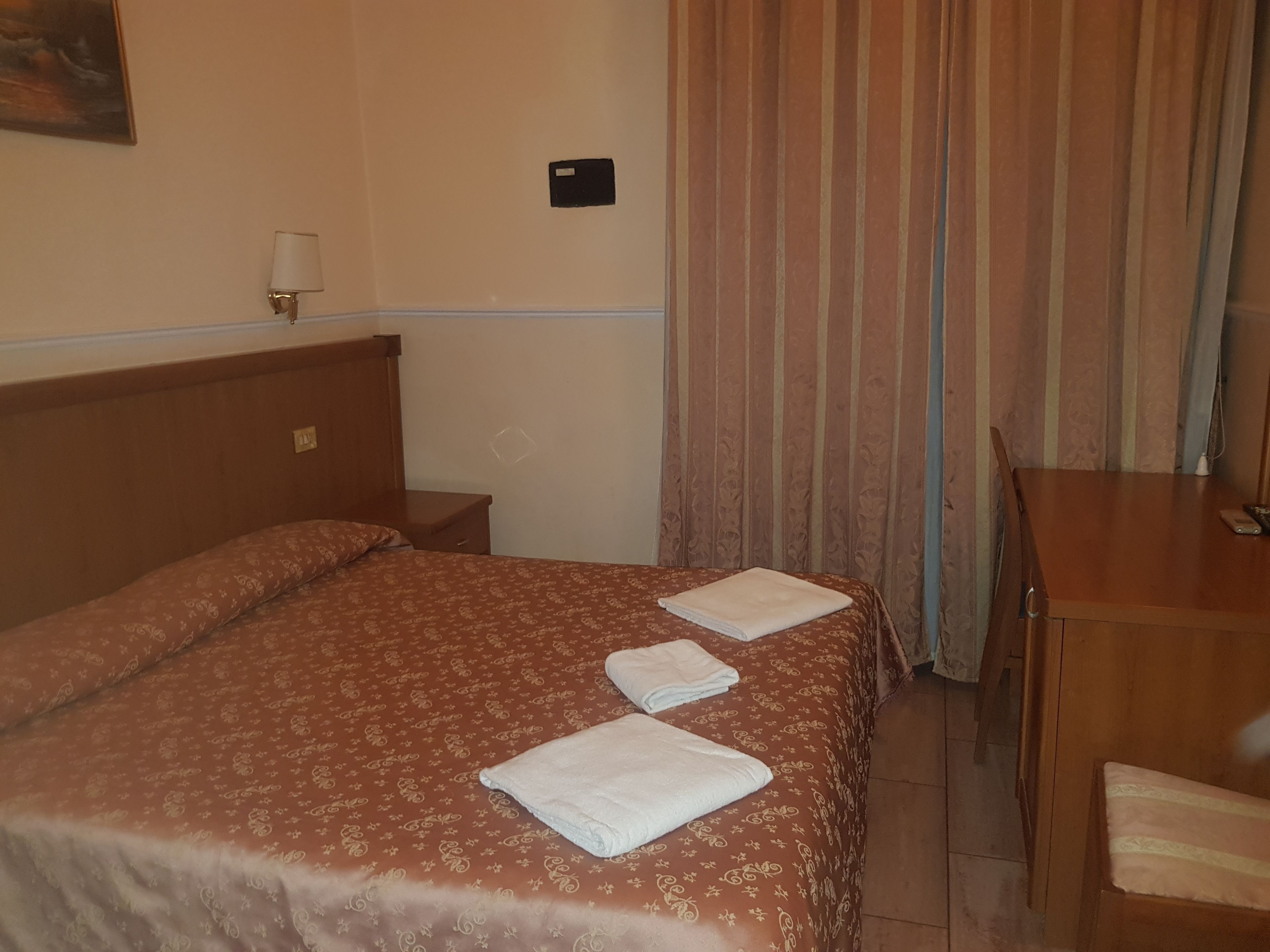 A hotel room with a bed, a nightstand, a desk, and a chair.