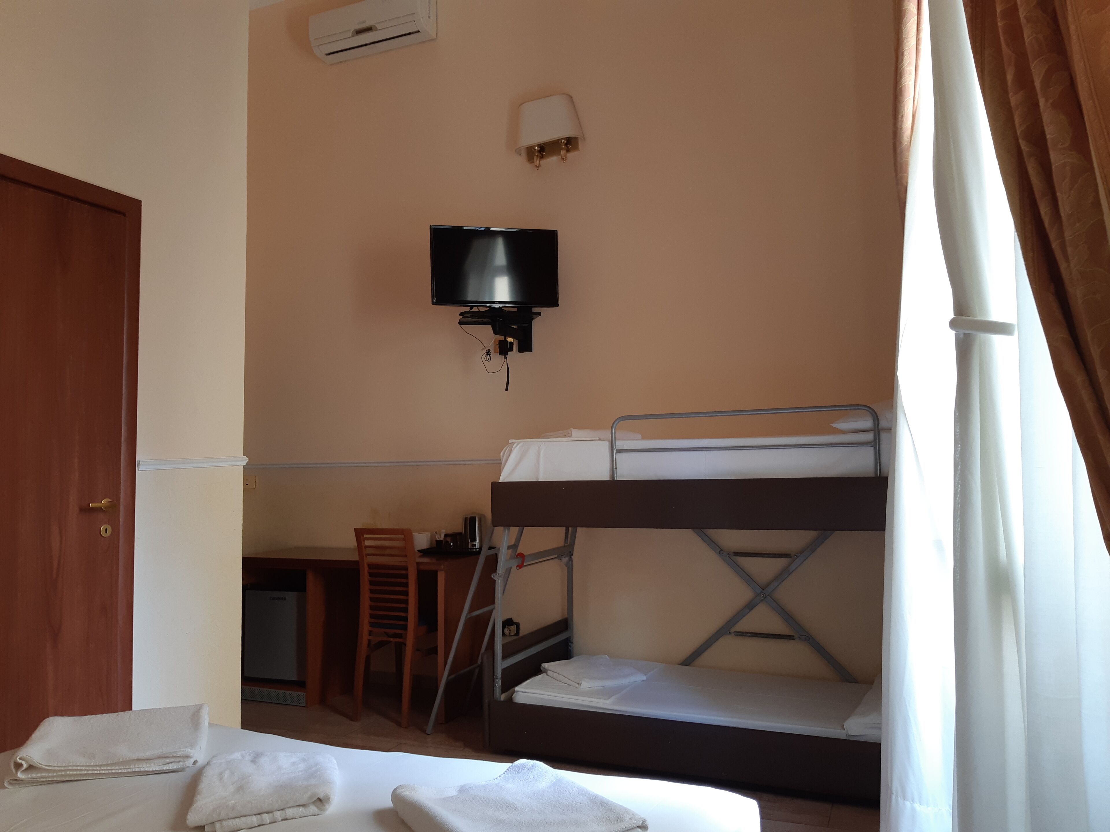 Een kamer met stapelbedden, een aan de muur bevestigde televisie, een bureau met stoel, en een deur.