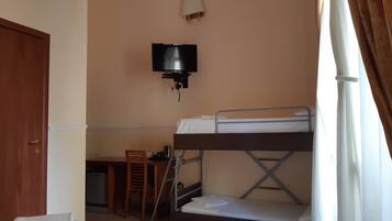 Een kamer met stapelbedden, een aan de muur bevestigde televisie, een bureau met stoel, en een deur.