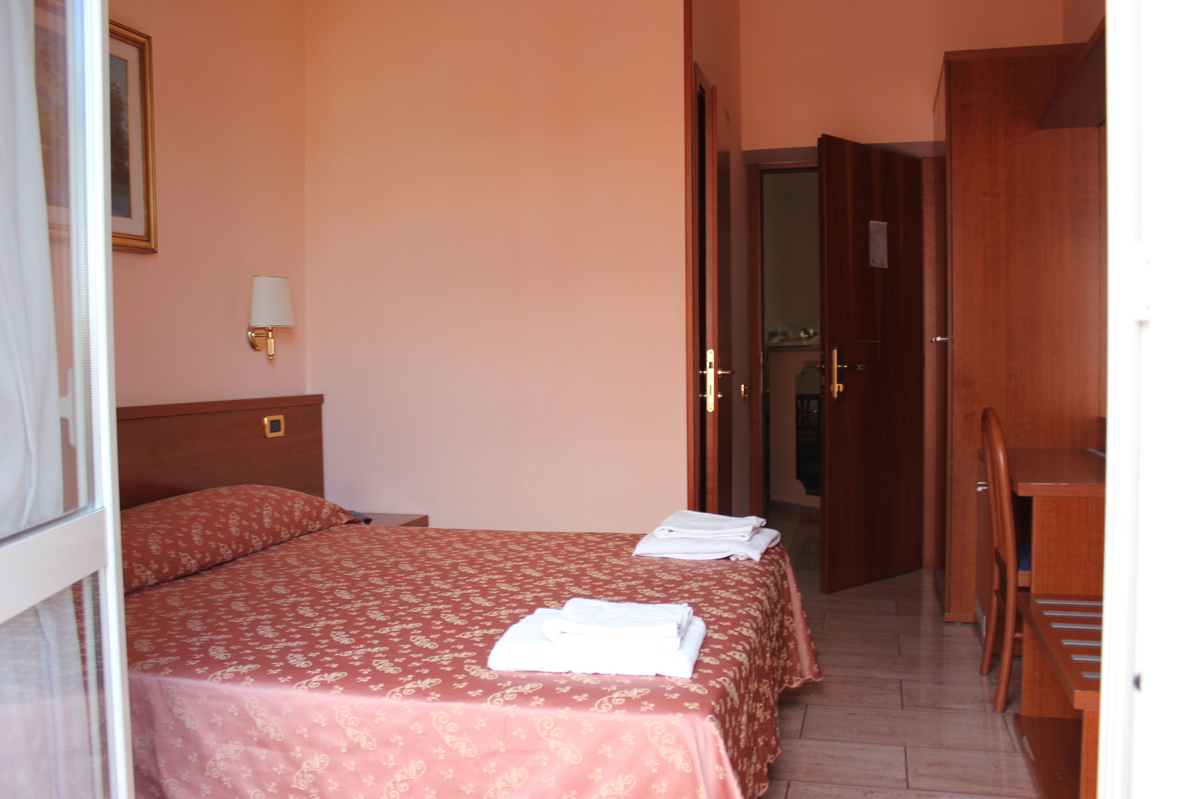 Une chambre d’hôtel avec un lit, une table de chevet, une lampe et un bureau en bois.