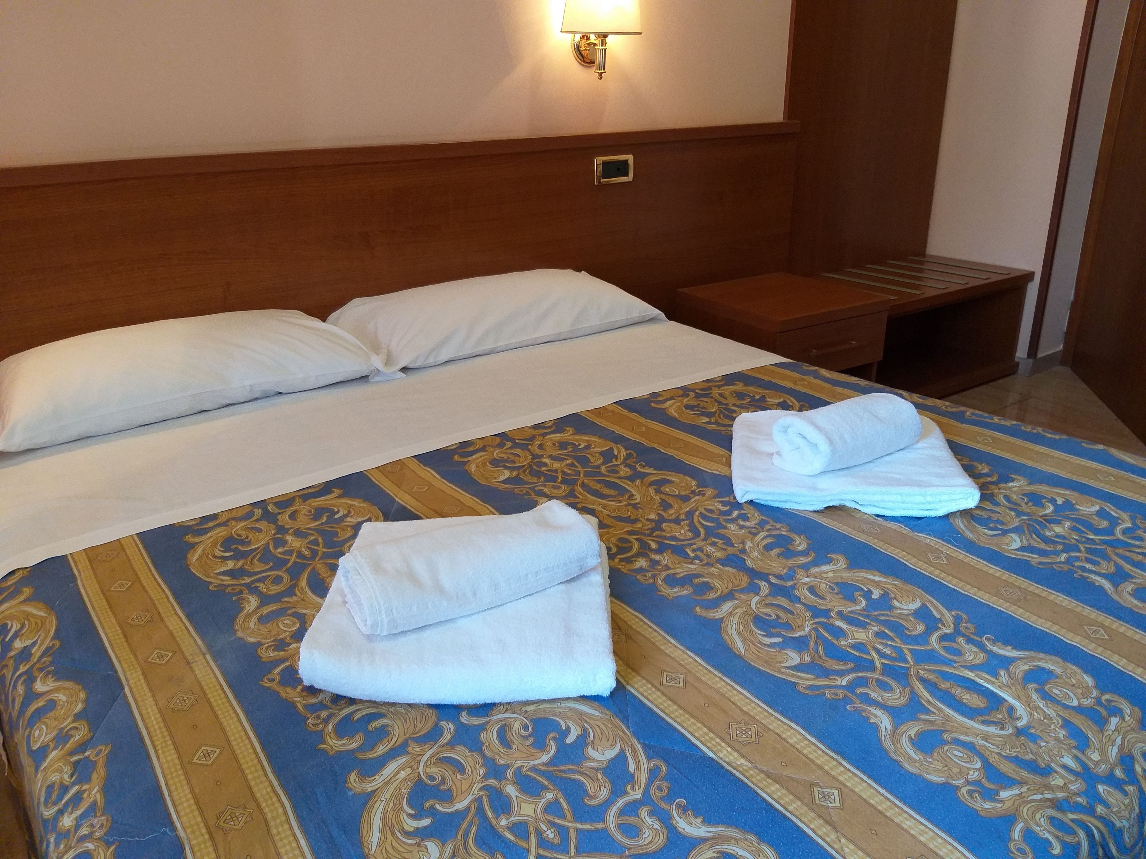 Une chambre d’hôtel avec un lit, deux oreillers, une table de chevet et une serviette pliée posée sur le lit.