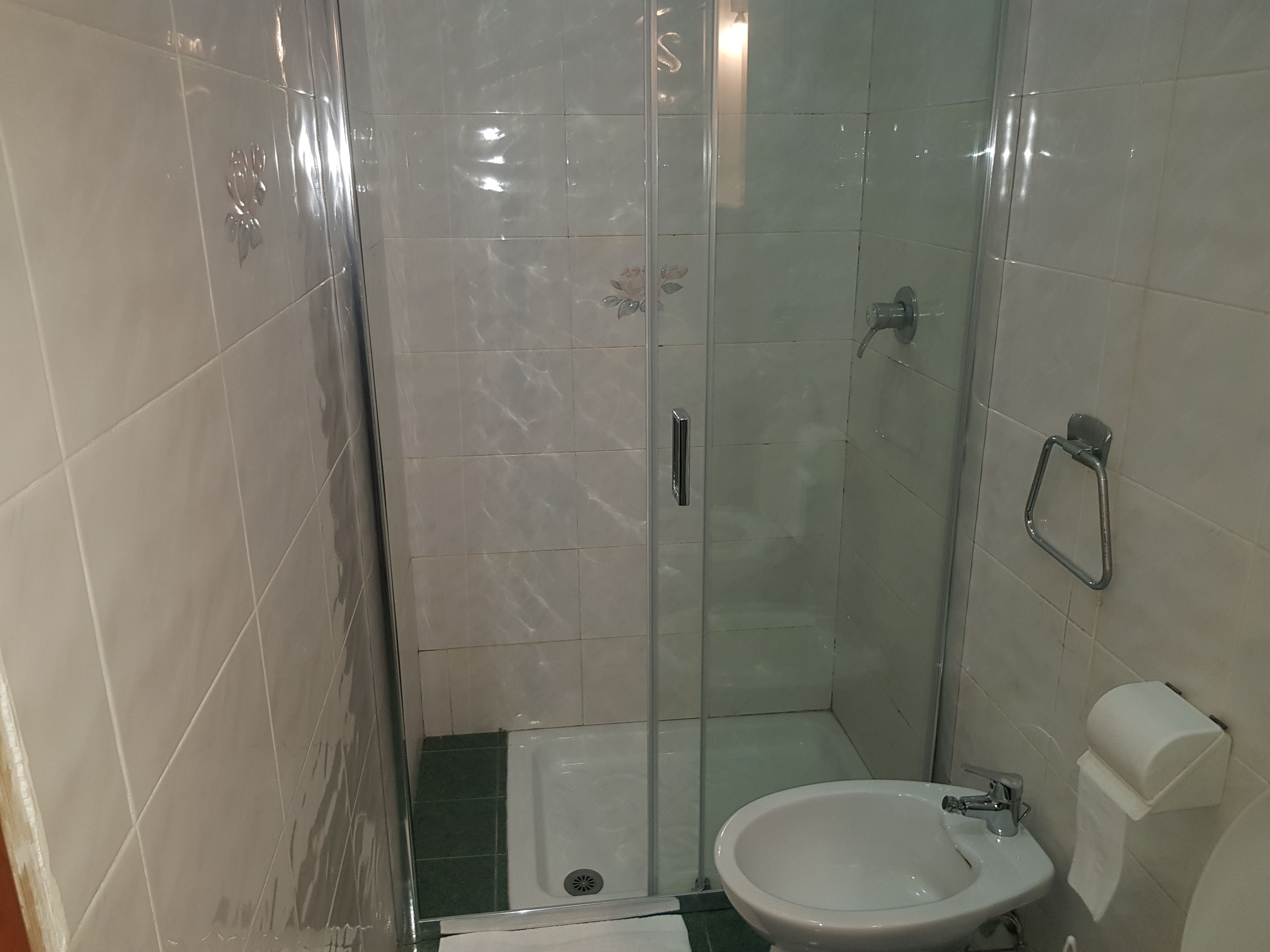 A small bathroom with a glass shower enclosure, a white sink, and a toilet.