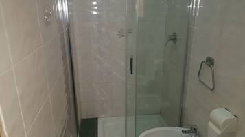 A small bathroom with a glass shower enclosure, a white sink, and a toilet.