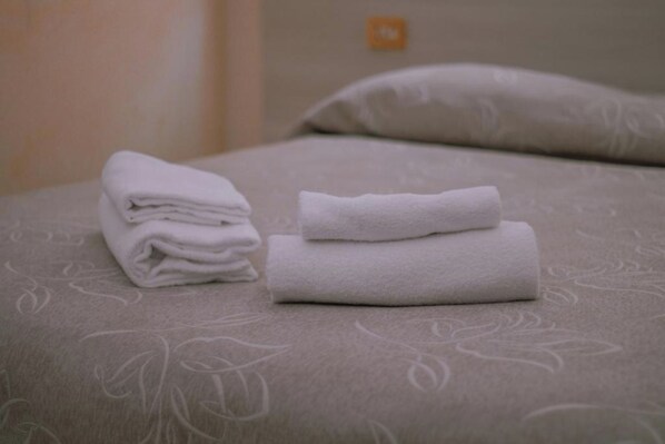 A neatly made bed with folded white towels and a pillow on a patterned bedspread. - Aristotele Hotel (Rome)