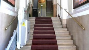 A grand staircase with marble steps and a red carpet leading to a door with a sign above it. - Aristotele Hotel (Rome)