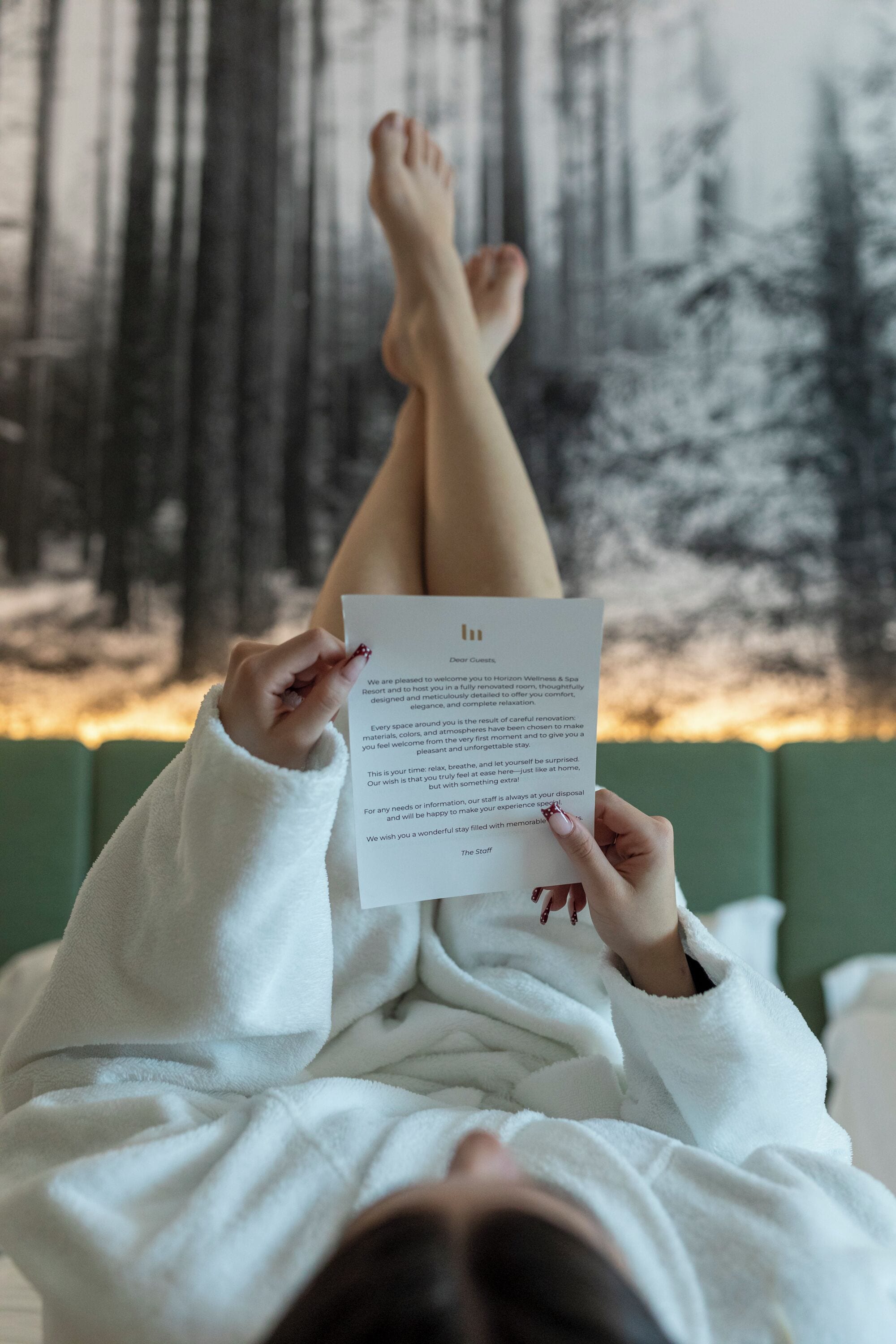 Een persoon ligt op een bed met een witte deken en houdt een stuk papier vast.