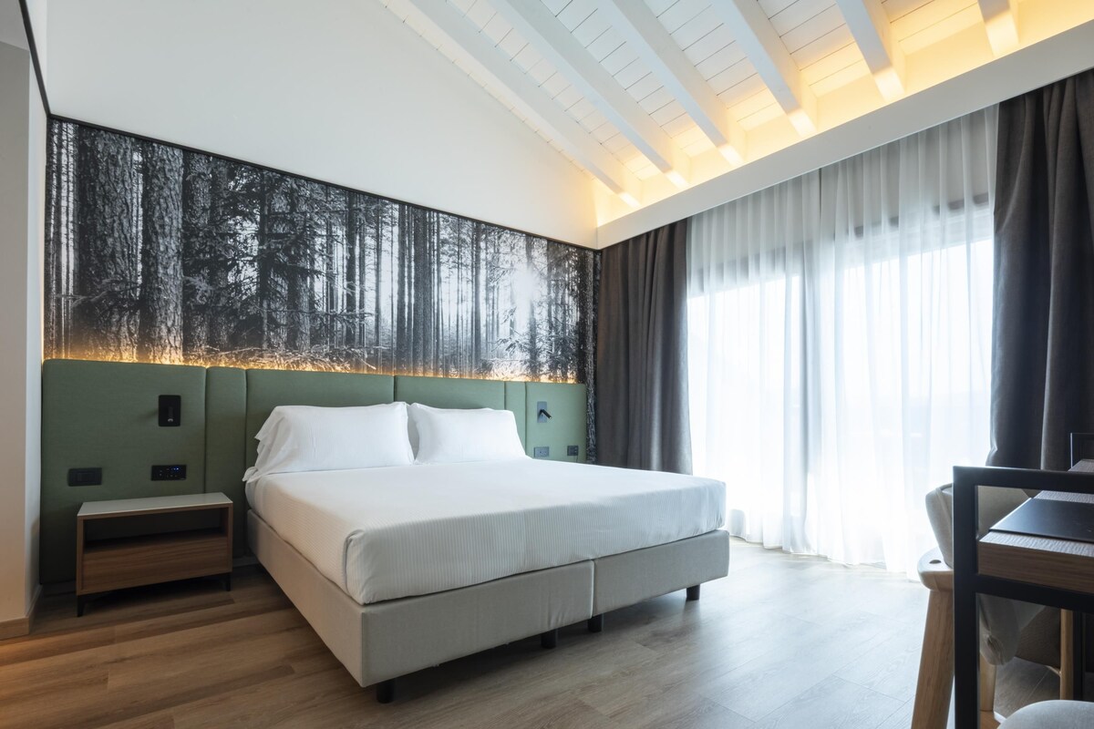 Un dormitorio moderno con una cama grande, una mesita de noche, un escritorio y un televisor montado en la pared.