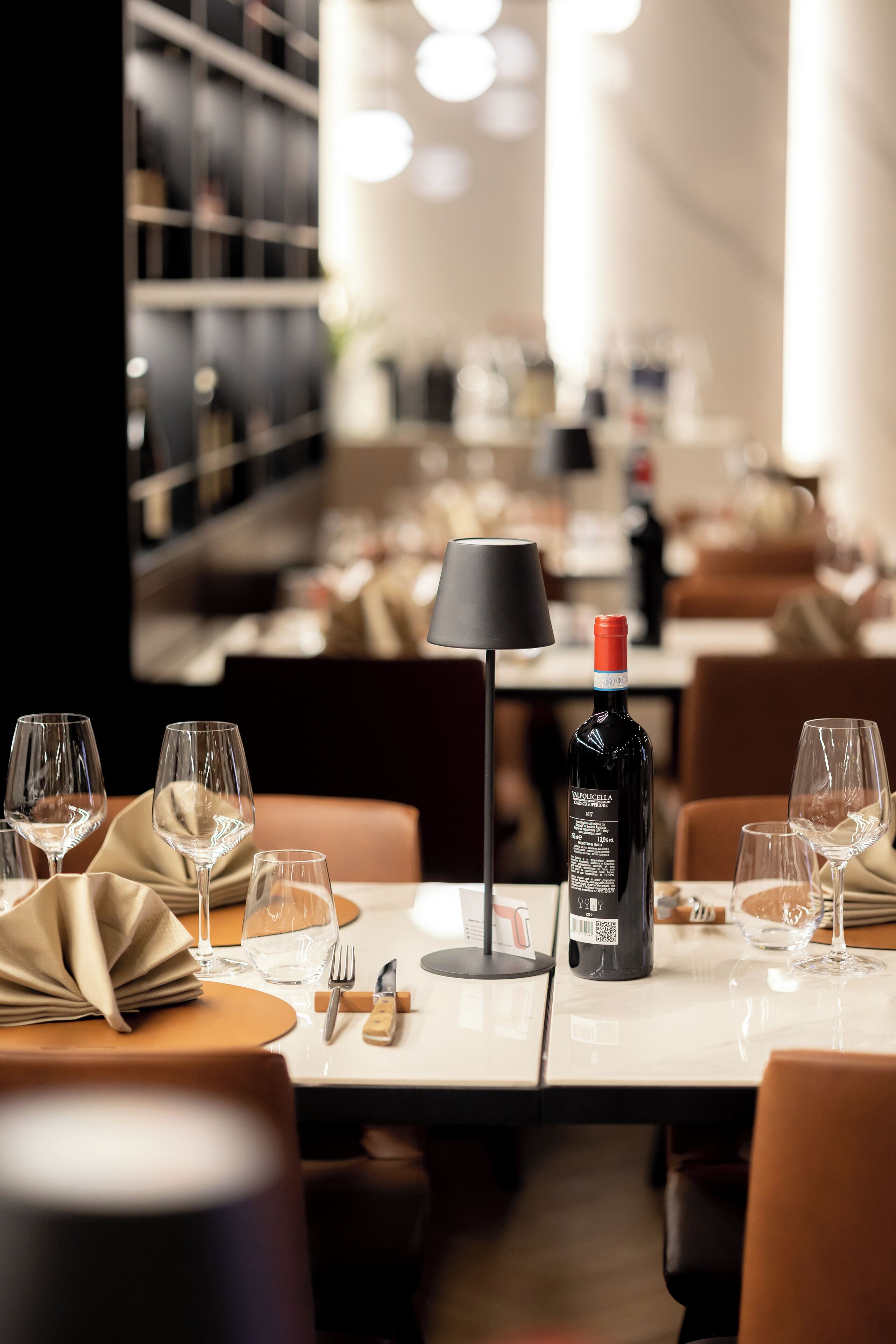 A restaurant setting with tables set for dining, including wine glasses, cutlery, and a bottle of wine.